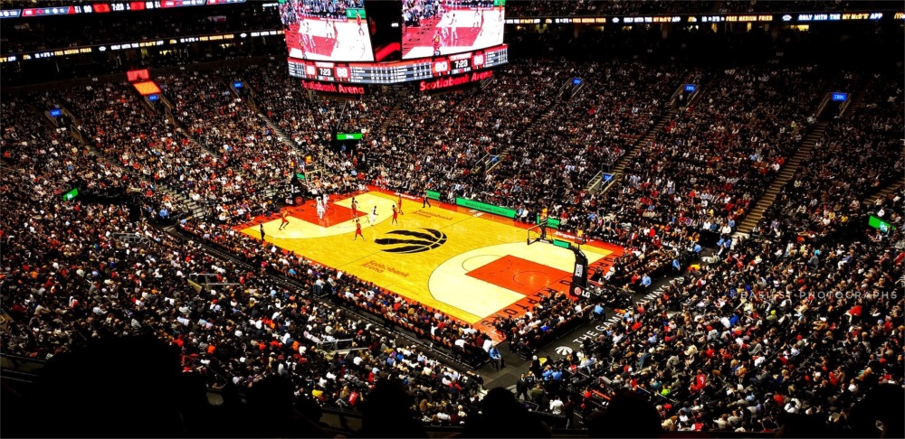 This is a photograph taken inside the Scotiabank Arena at 40 Bay Street Toronto, Ontario, Canada. Fans in the croweded arena are watching a basketball game.