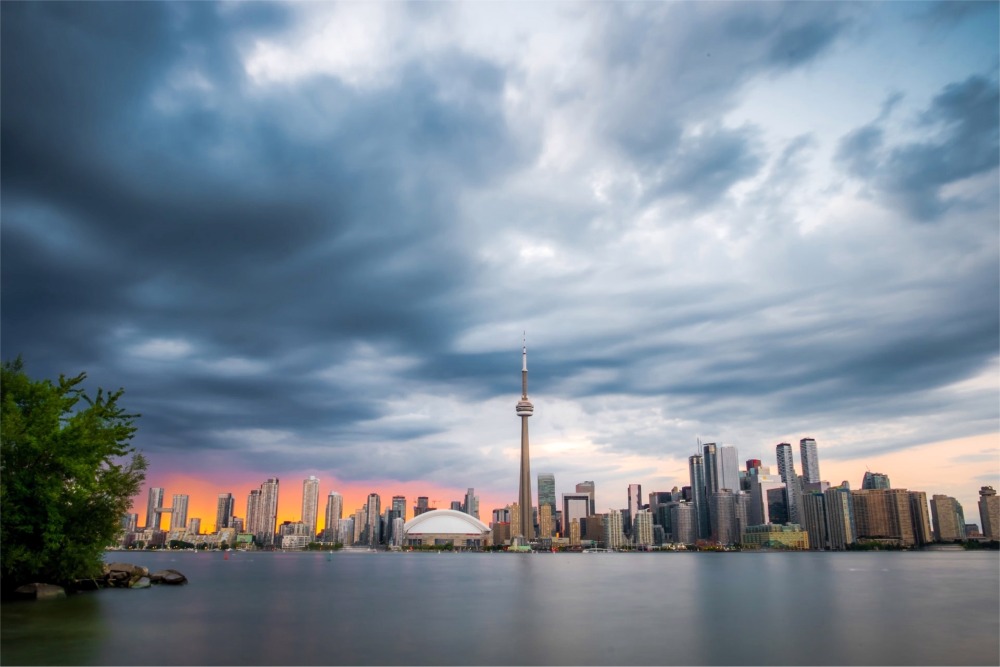 This is a photograph of the Toronto skyline at sunset from Centre Island. The CN Tower and Rogers Centre feature in the middle of the photo.