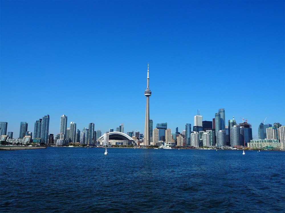 Photograph of the Toronto skyline with Lake Ontario in the foreground. It is a bright sunny day - Roger's Centre and the CN Tower feature in the middle of the image.