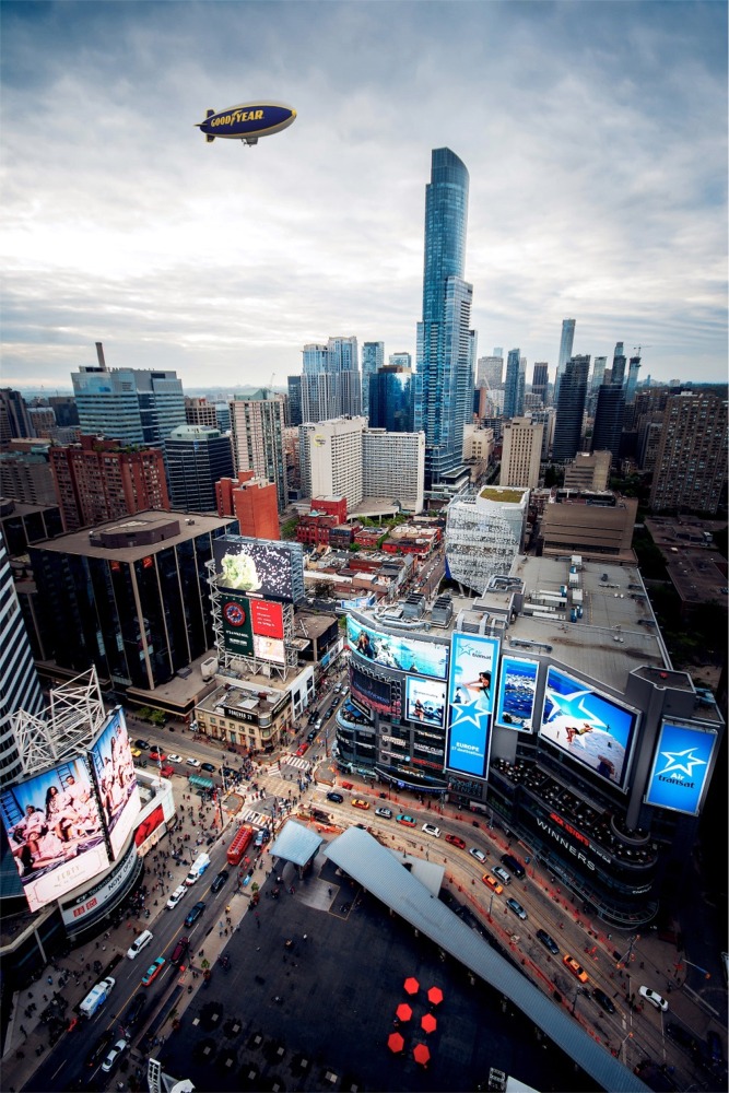 Photograph of a Toronto Ontario downtown cityscape with Yonge-Dundas Square in the foreground and a Goodyear blimp overhead.